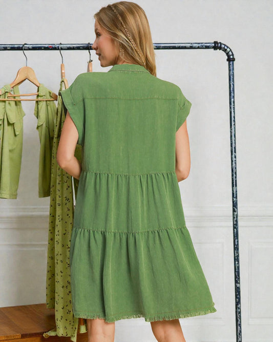 Woman wearing a green dress standing in front of a rack with more dresses.