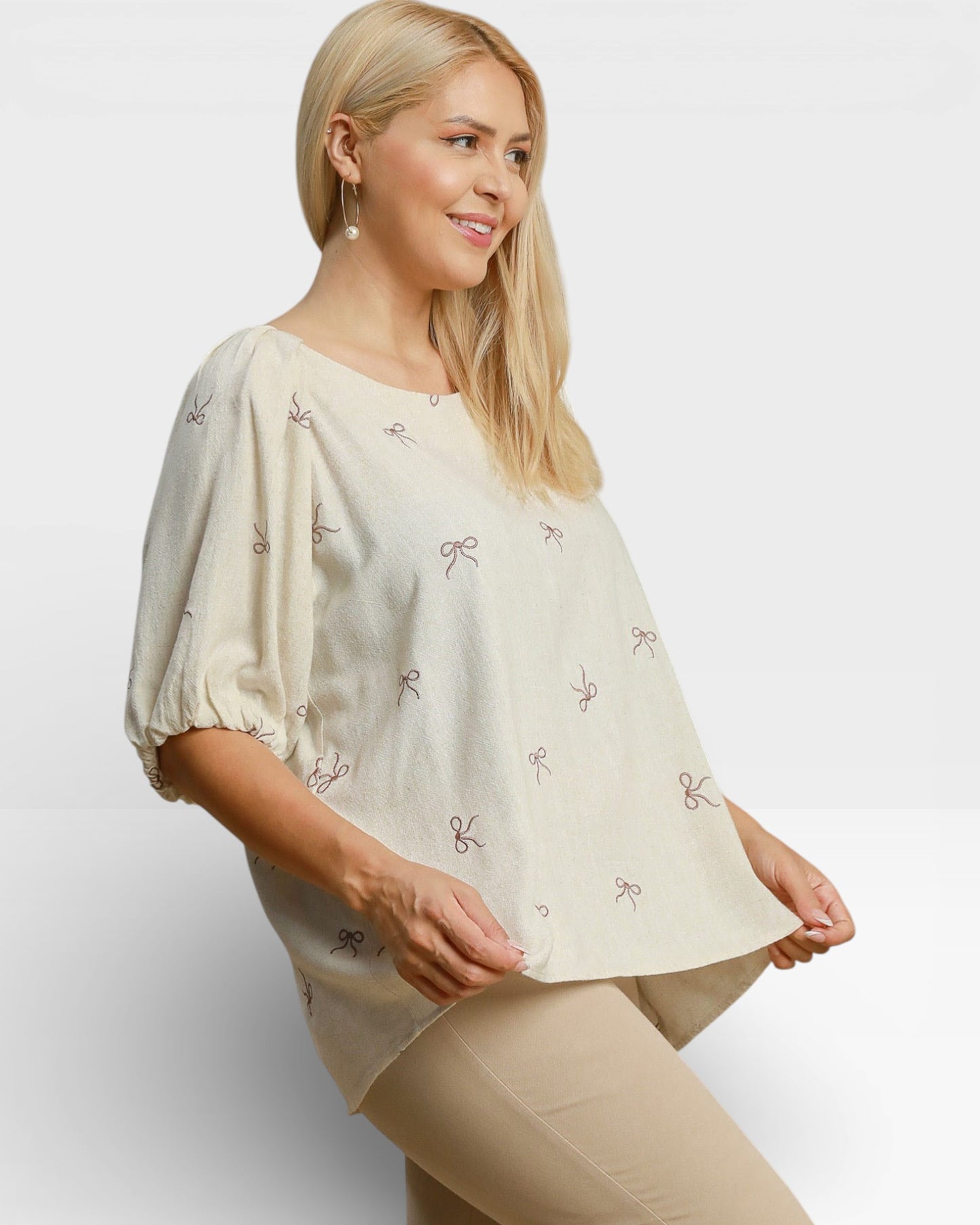 Woman wearing a beige blouse with bow patterns on a plain background