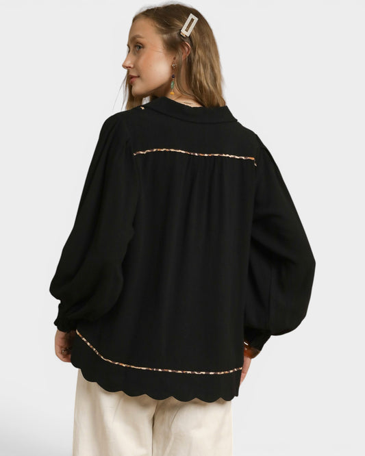 Person wearing a black sweater with scalloped hem on a white background