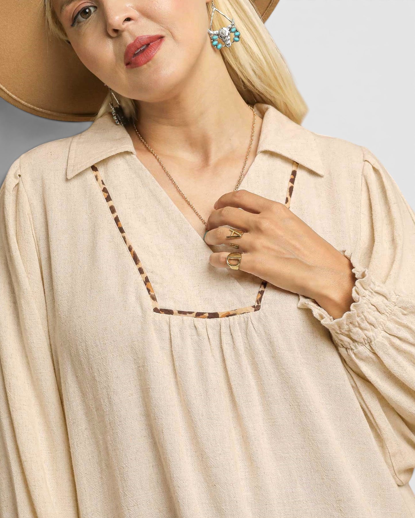 Woman wearing a beige blouse with a necklace and hat against a neutral background