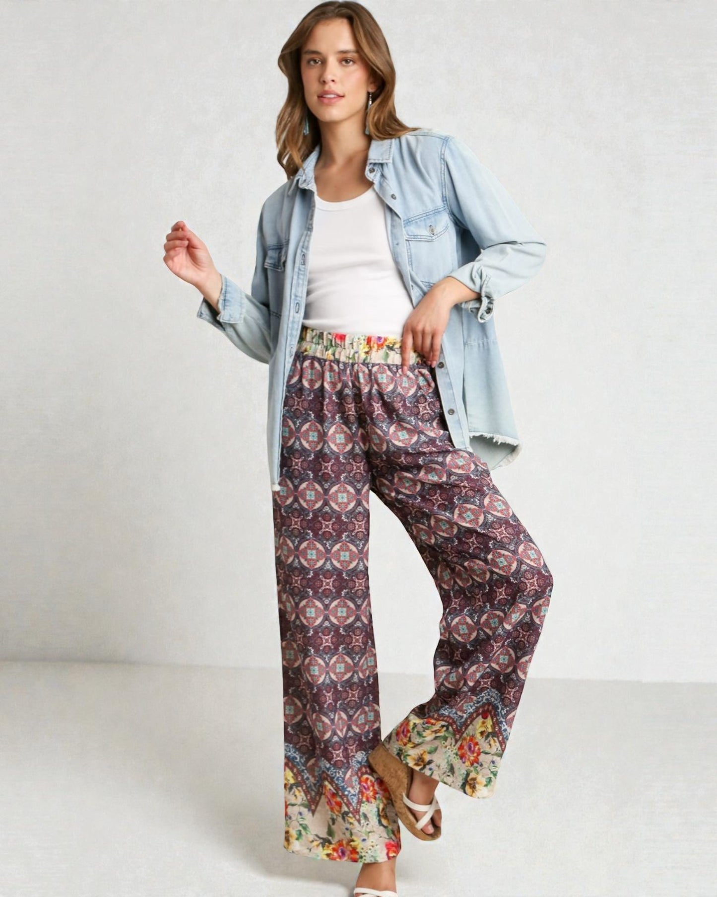 Woman wearing a denim jacket, white top, and patterned pants on a white background