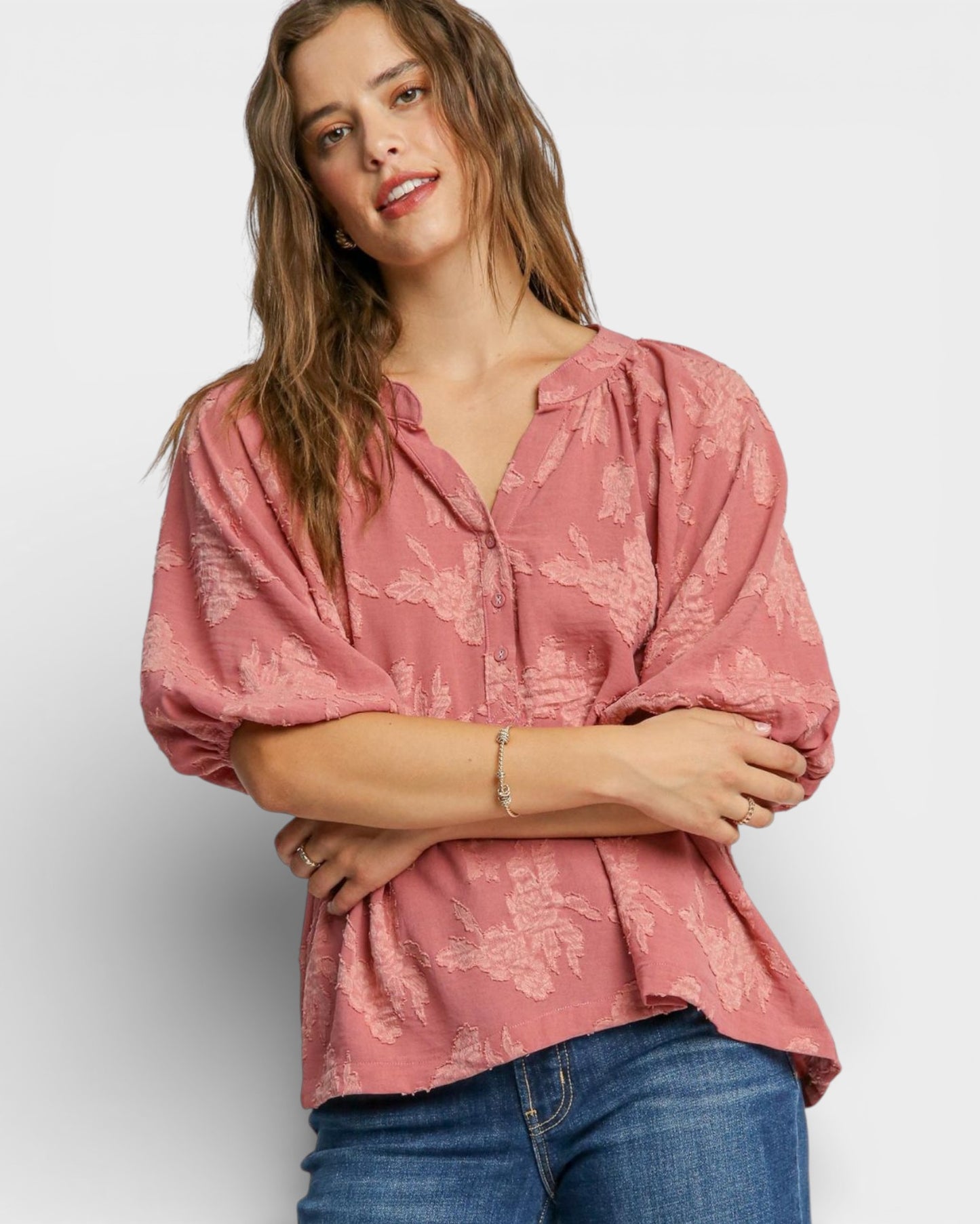 Woman wearing a pink floral blouse and blue jeans against a white background