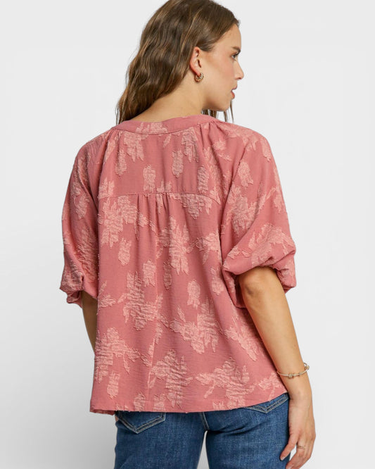 Woman wearing a pink patterned blouse and blue jeans on a white background