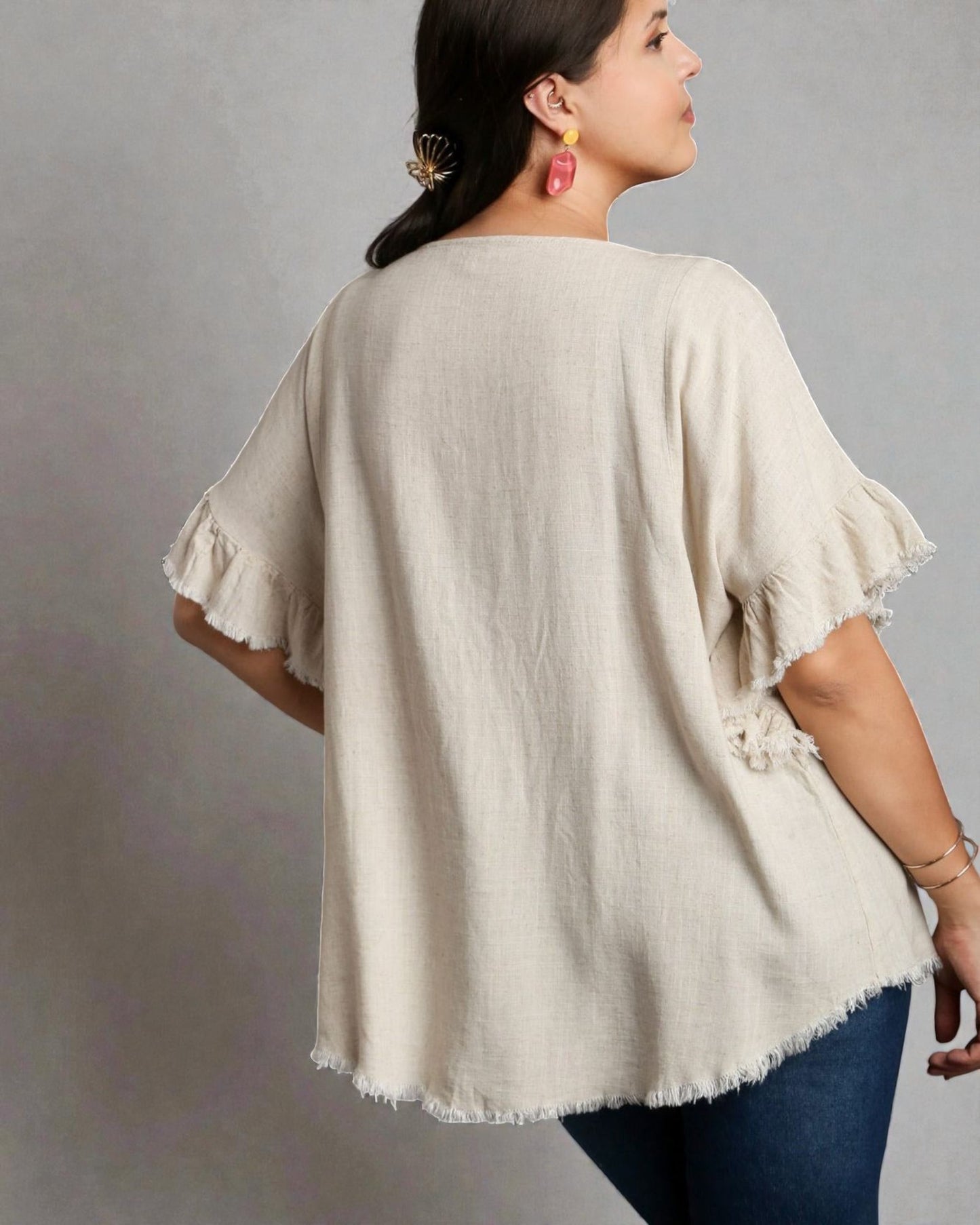 Woman wearing a beige blouse with ruffled sleeves on a gray background