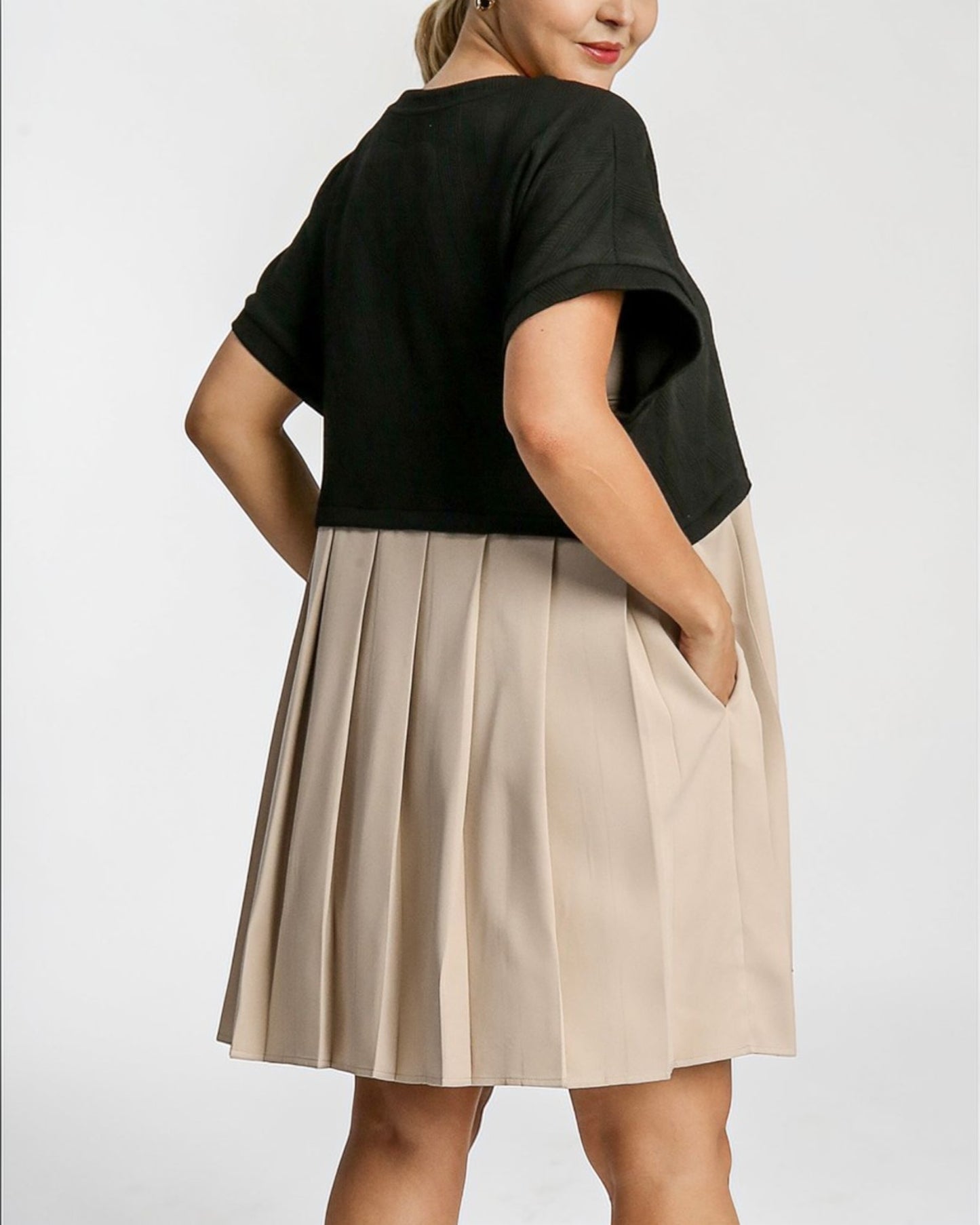 Person wearing a black top and beige pleated skirt on a white background