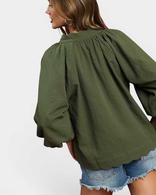 Woman wearing an olive green blouse with a plain background