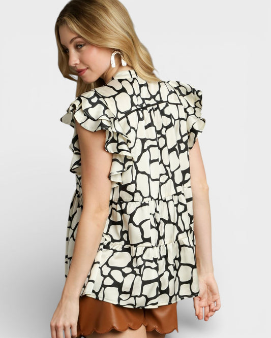 Woman wearing a patterned blouse with ruffled sleeves on a plain background