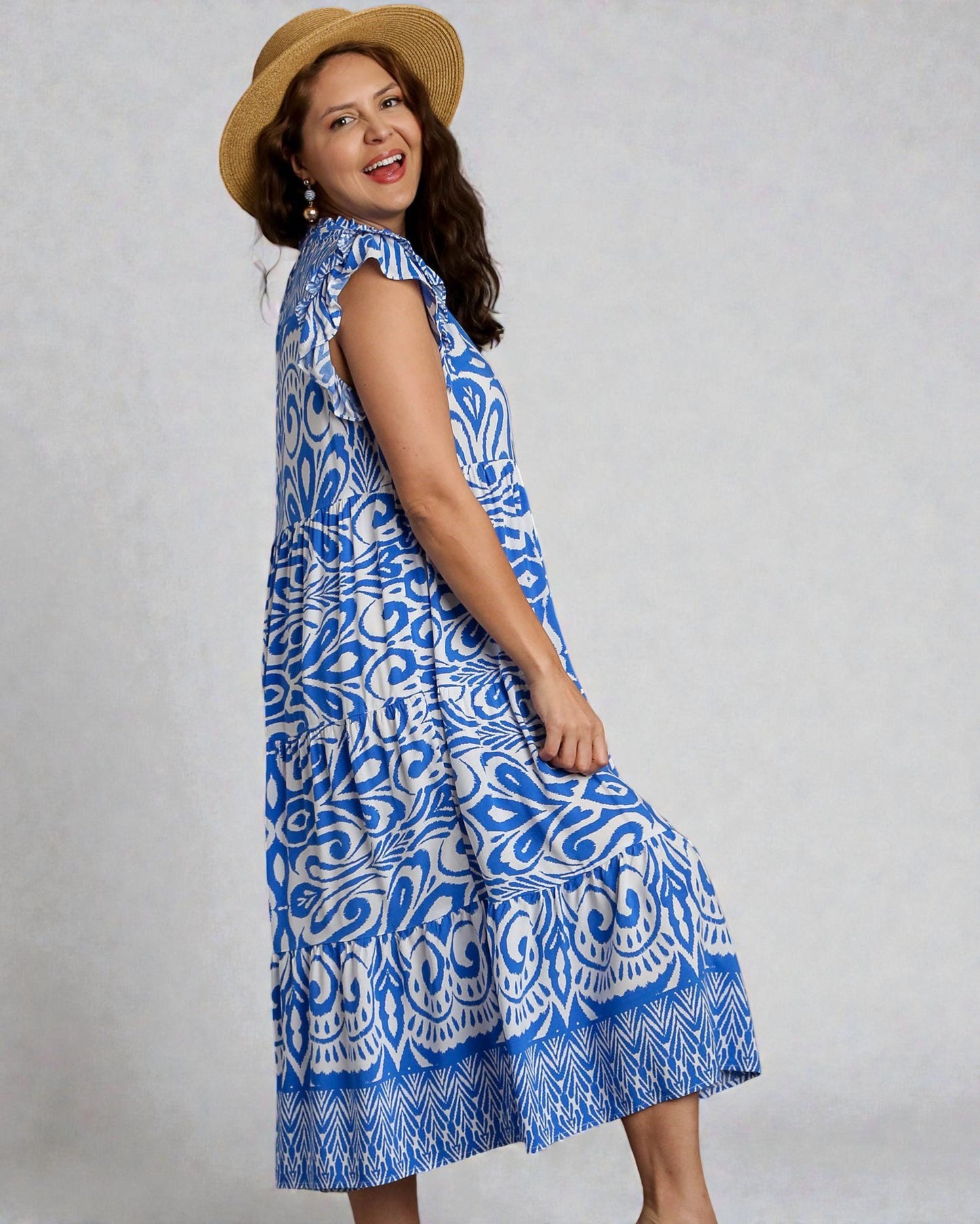 Woman wearing a blue patterned dress and straw hat against a gray background