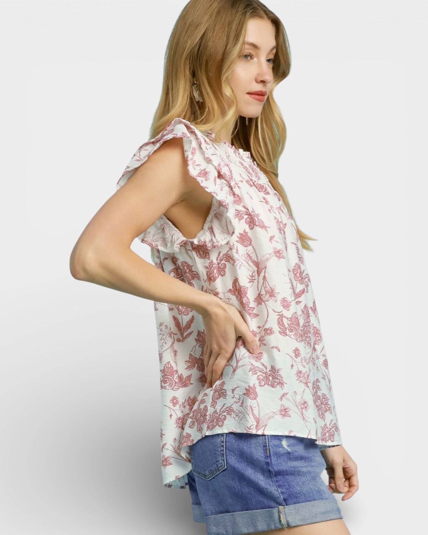 Woman wearing a floral top and denim shorts on a plain background