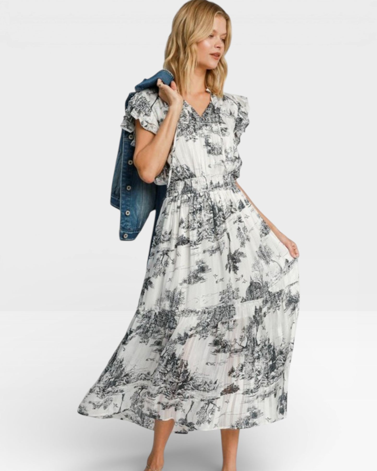 Woman wearing a floral dress holding a denim jacket on a white background