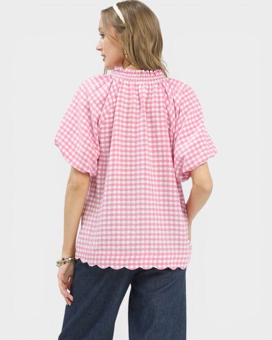 Woman wearing a pink gingham blouse and dark pants on a white background