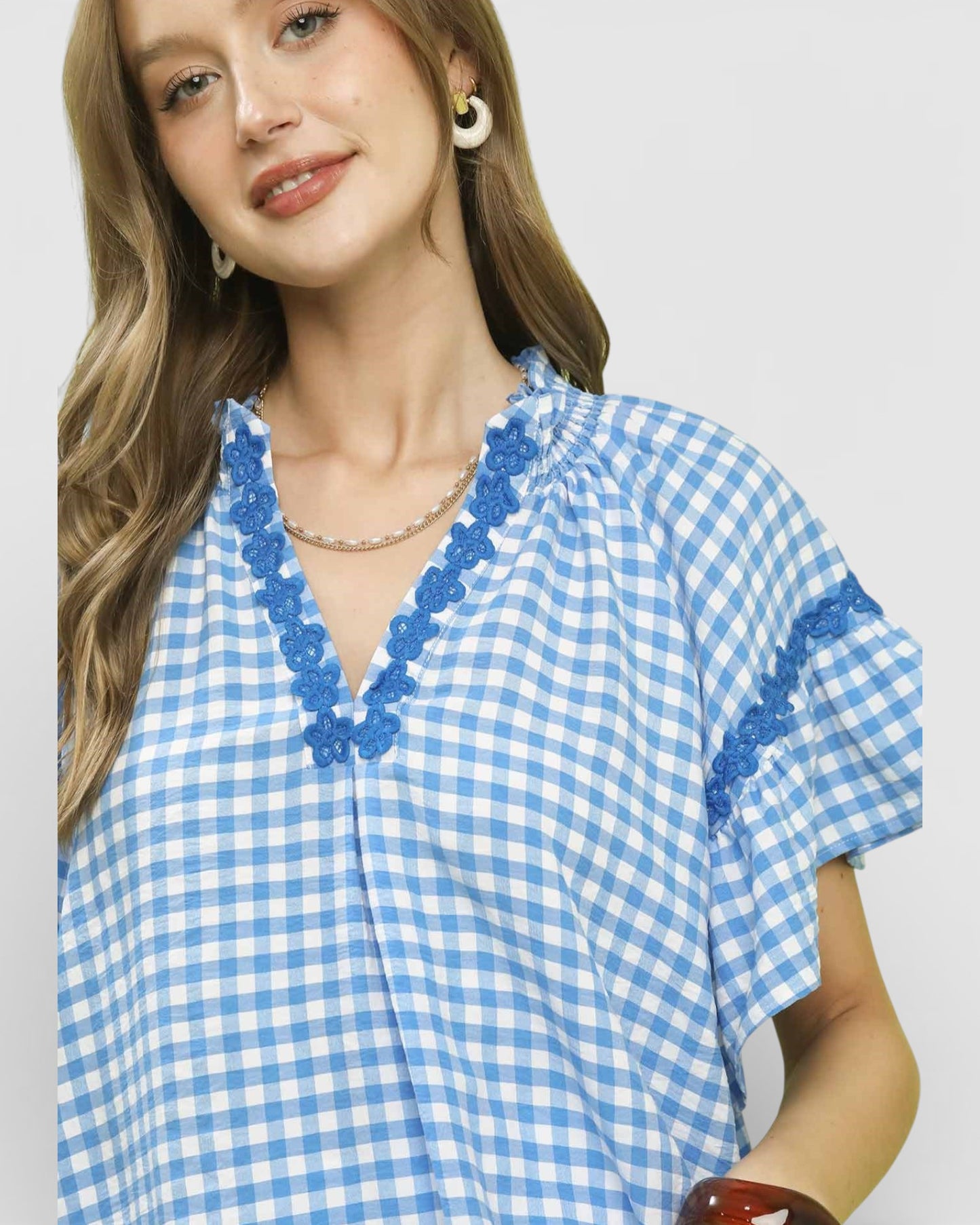 Woman wearing a blue and white checkered dress with decorative trim on a plain background