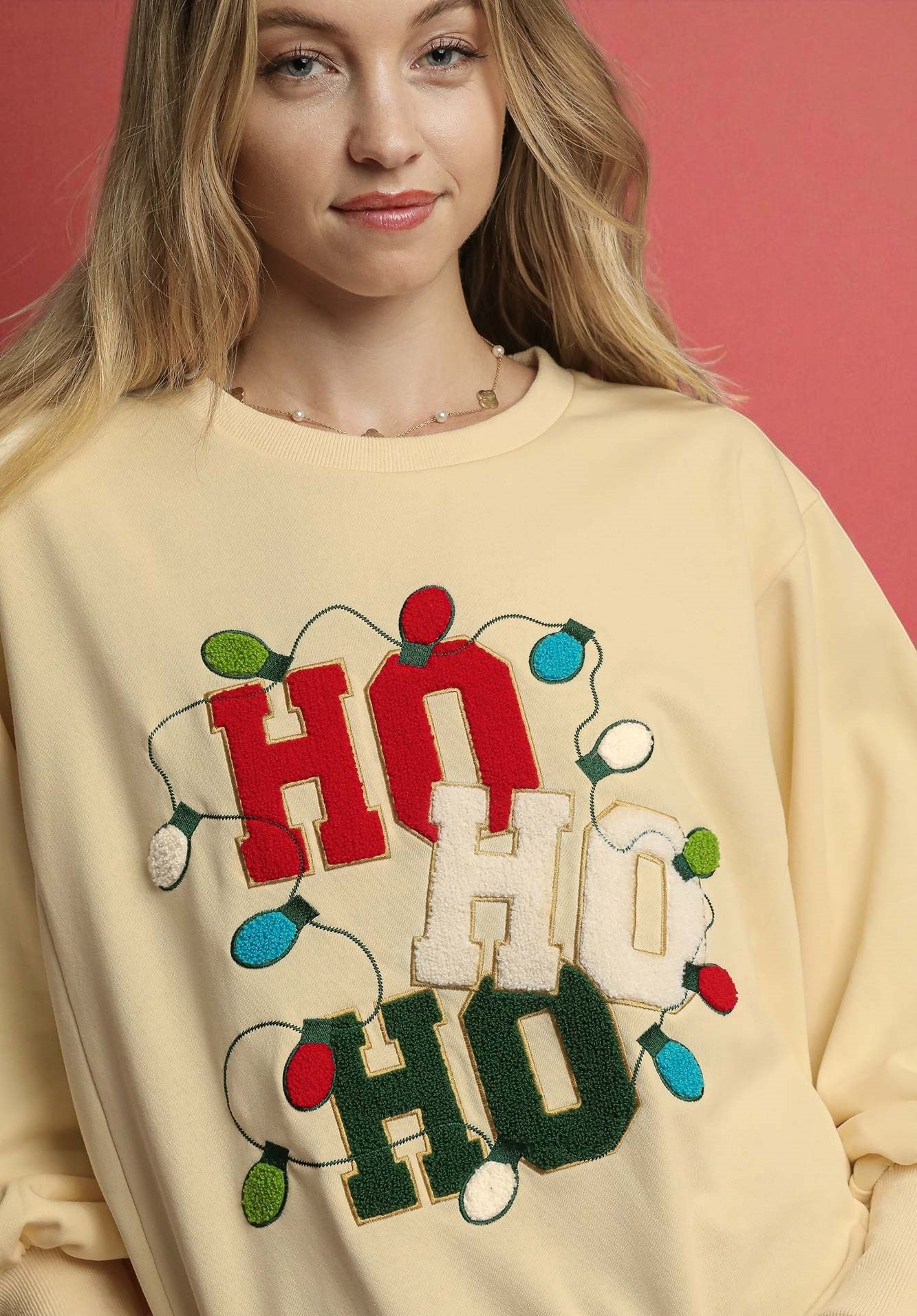 Person wearing a cream sweatshirt with 'HO HO HO' text and Christmas lights design.