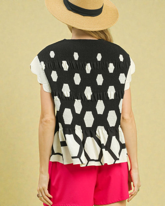 Person wearing a black and white patterned sleeveless top with pink shorts on a beige background