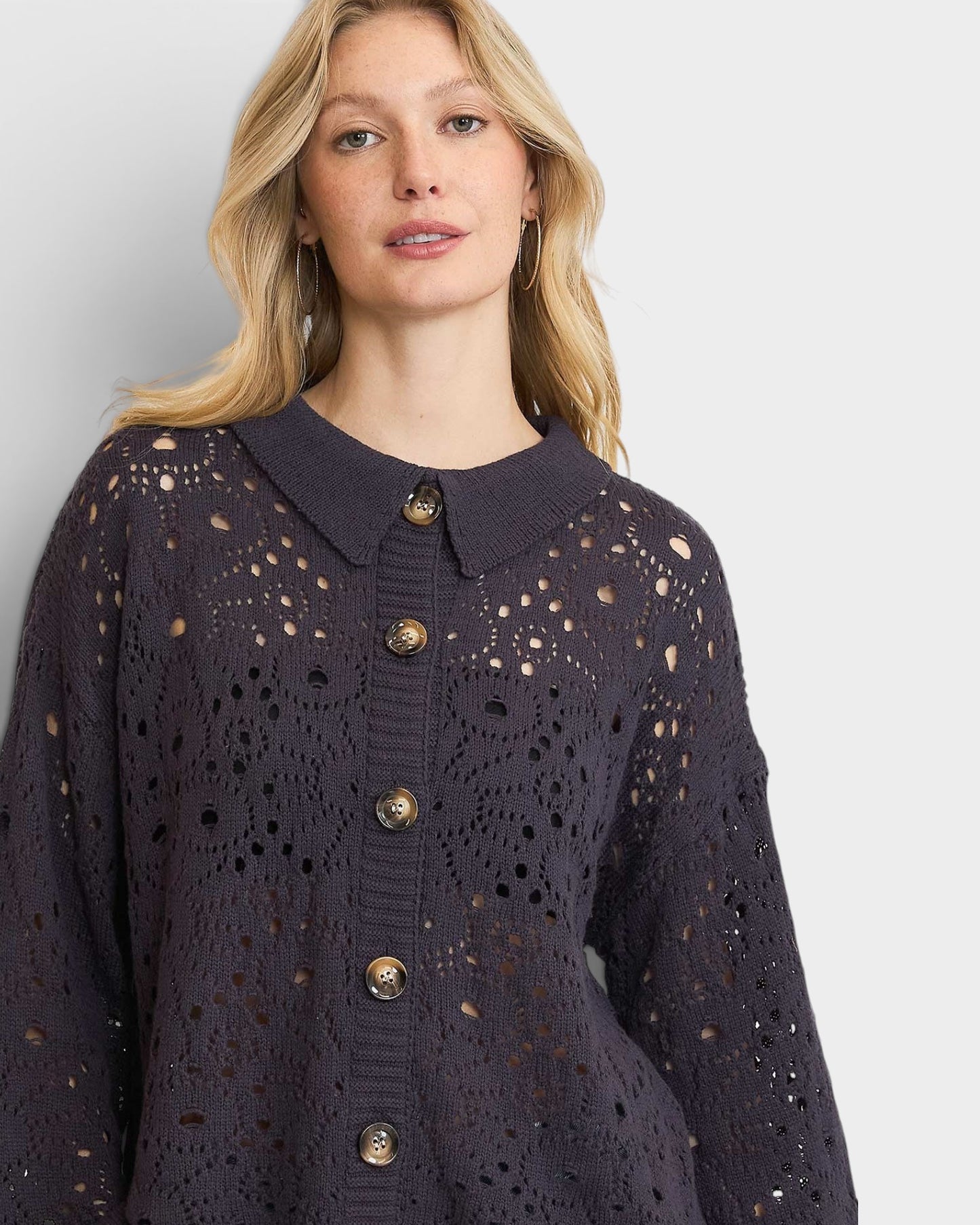 Woman wearing a dark blue lace cardigan with gold buttons on a light gray background