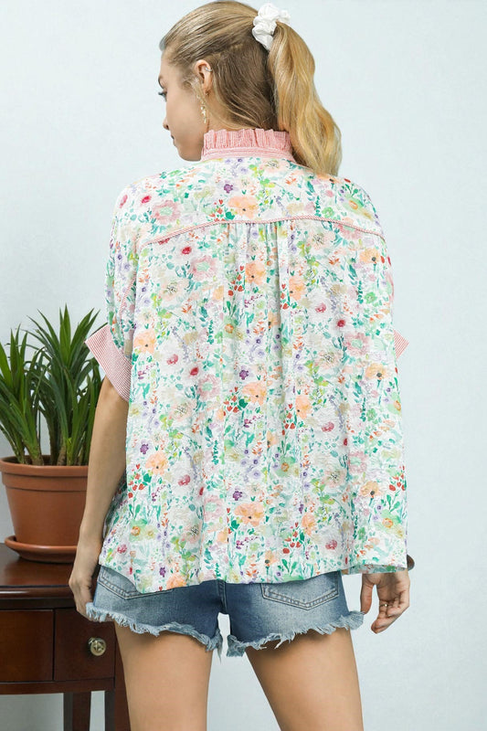 Woman wearing a floral blouse and denim shorts against a light background