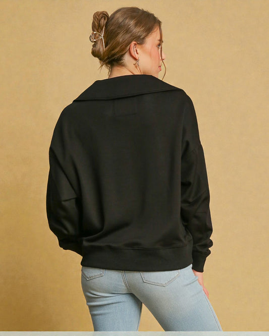 Person wearing a black sweater and light blue jeans against a beige background