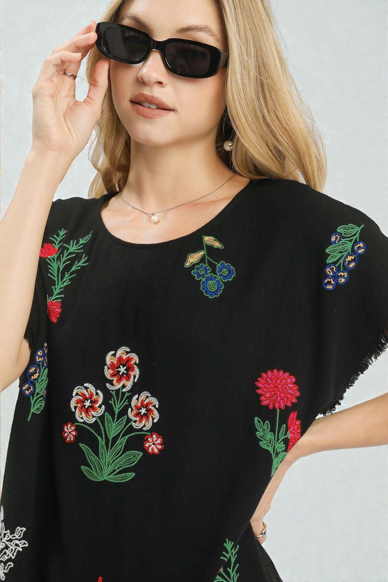 Woman wearing a black top with colorful floral embroidery against a light gray background