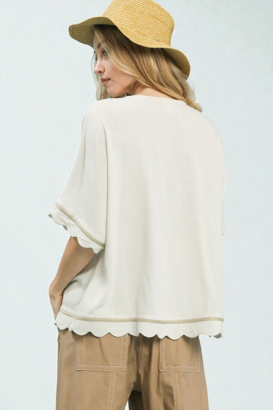 Woman wearing a beige hat and white blouse with scalloped hem on a light gray background