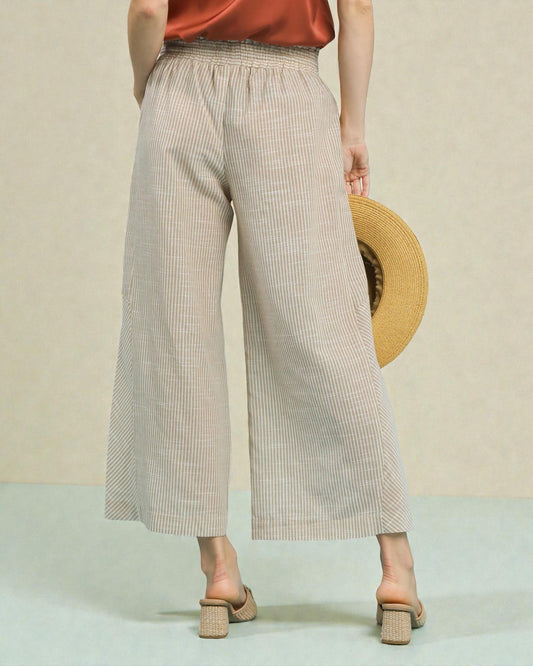 Person wearing beige checkered wide-leg pants holding a straw hat against a neutral background
