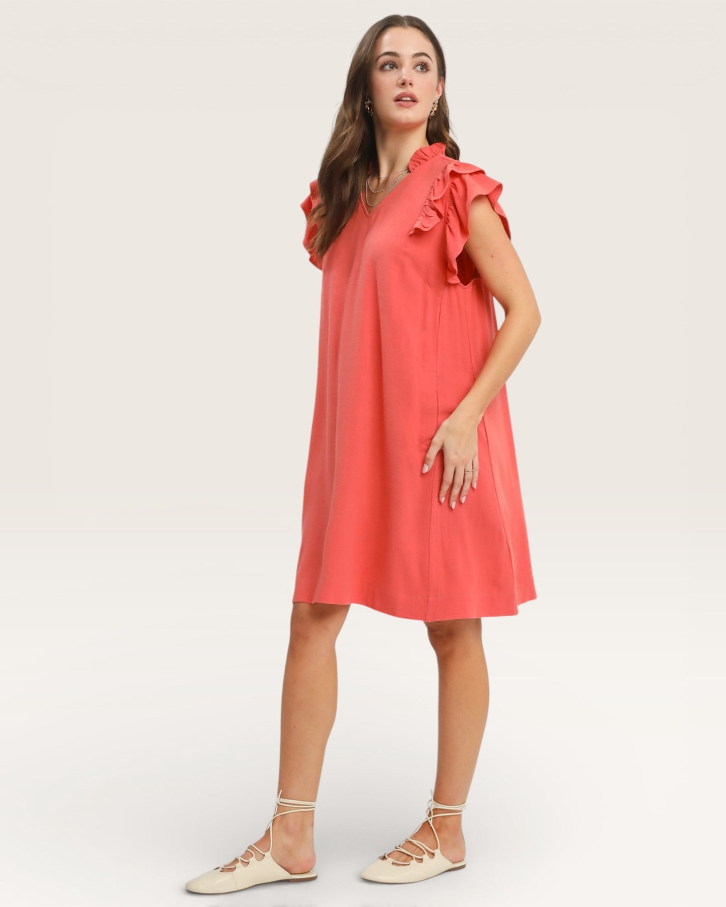 Woman wearing a coral dress with ruffled shoulders on a white background