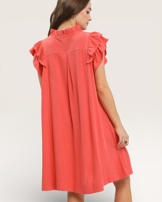 Coral dress with ruffled shoulders on a plain background