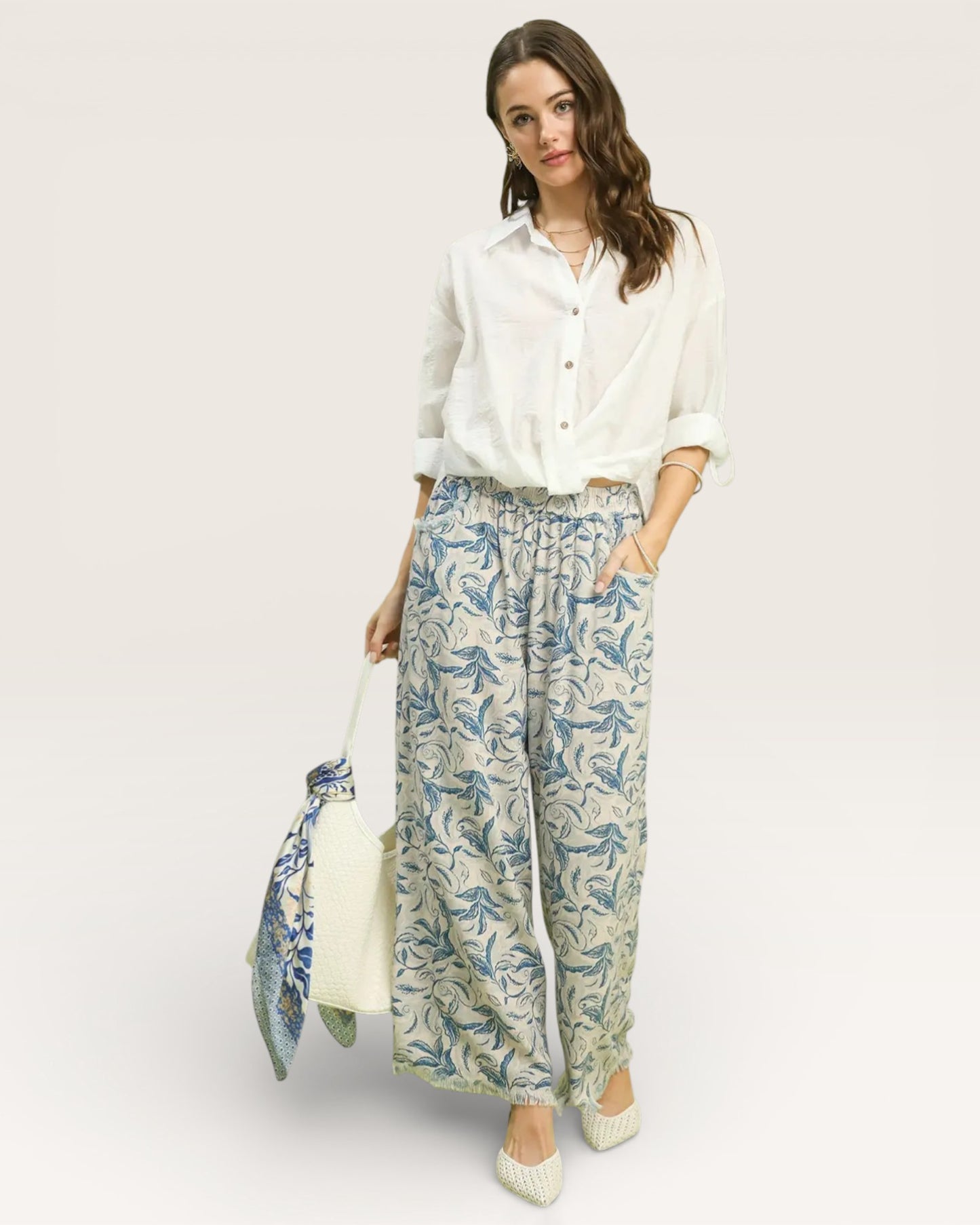 Woman wearing a white blouse and patterned pants with a white background