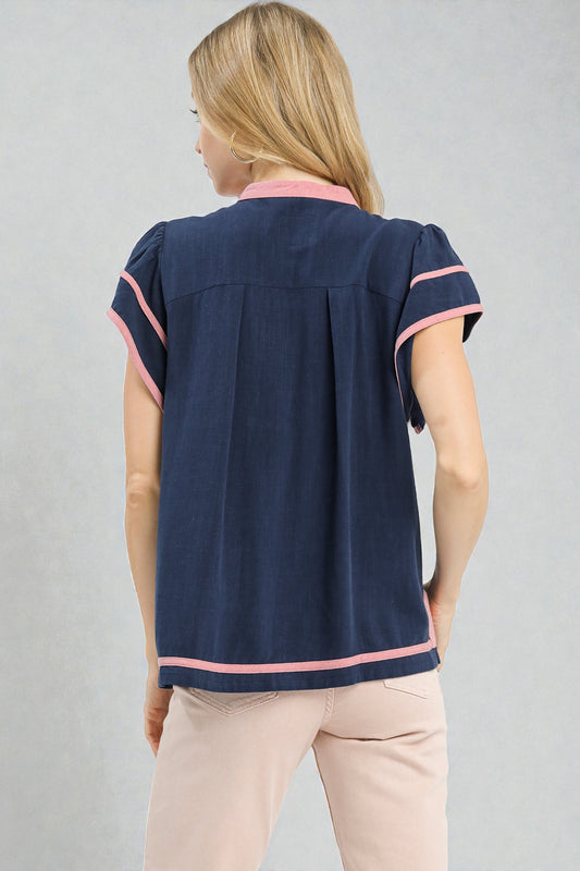 Woman wearing a navy blue blouse with pink accents on a gray background