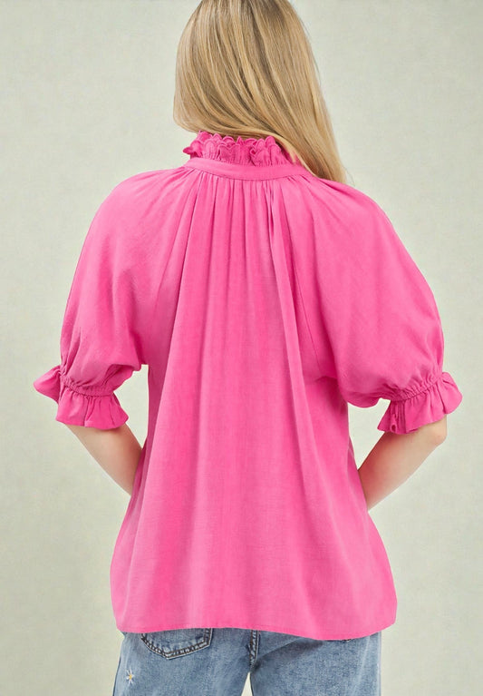 Person wearing a bright pink blouse with ruffled details on a plain background