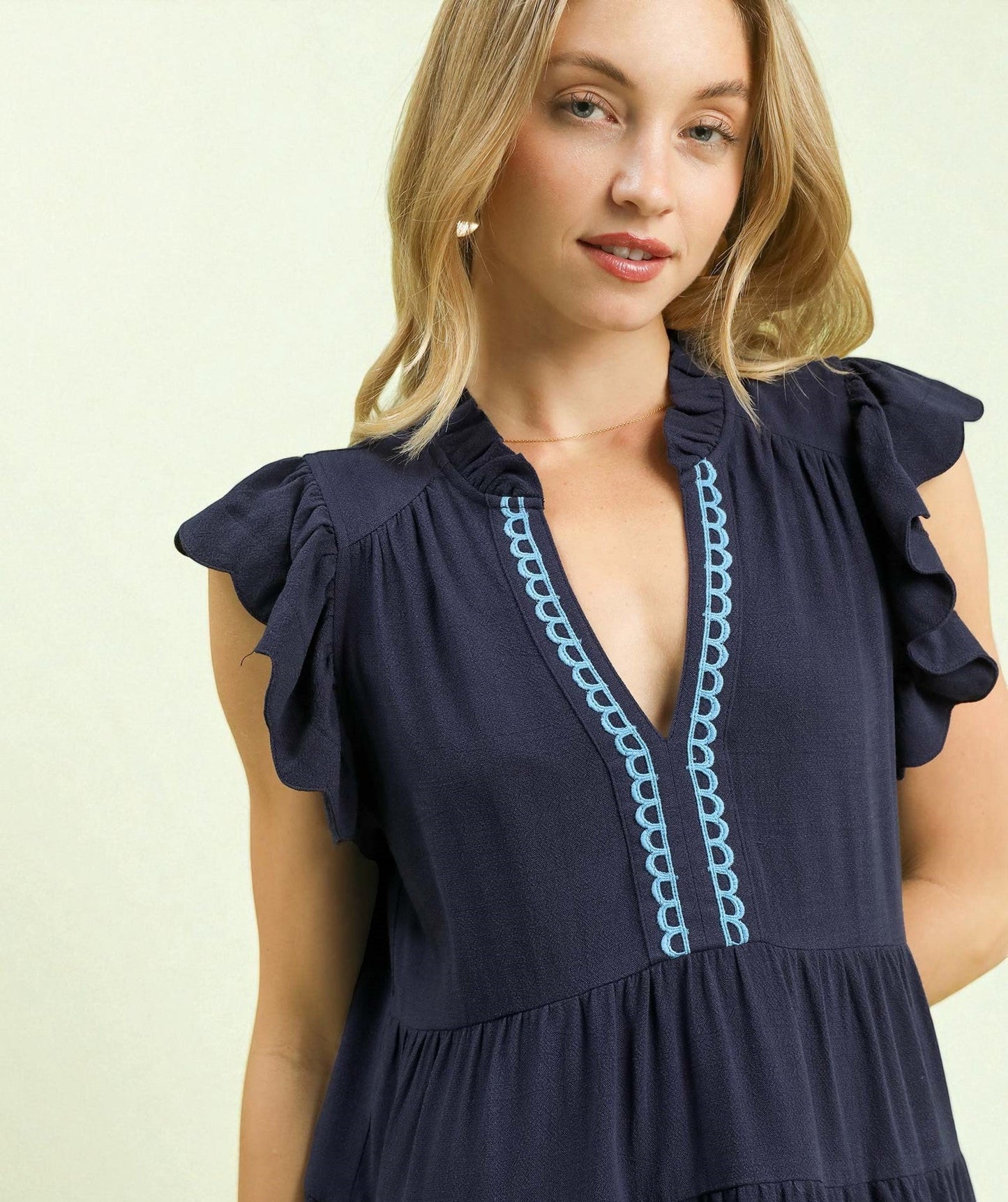 Woman wearing a navy dress with blue embroidery on a light background