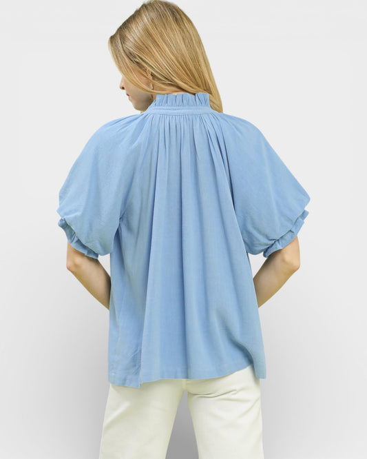 Woman wearing a light blue blouse with puff sleeves on a plain background