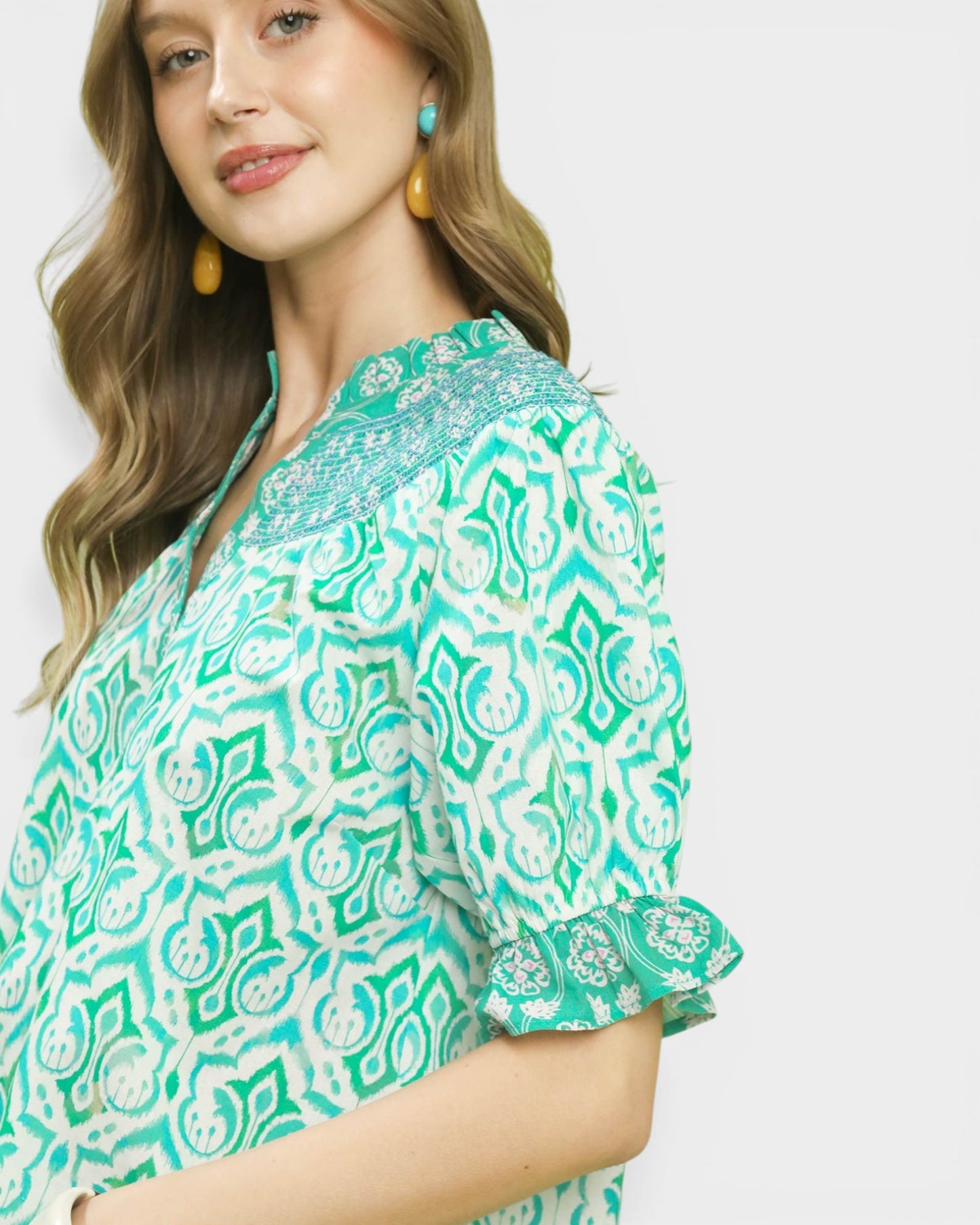 Woman wearing a green and white patterned blouse with ruffled sleeves on a plain background