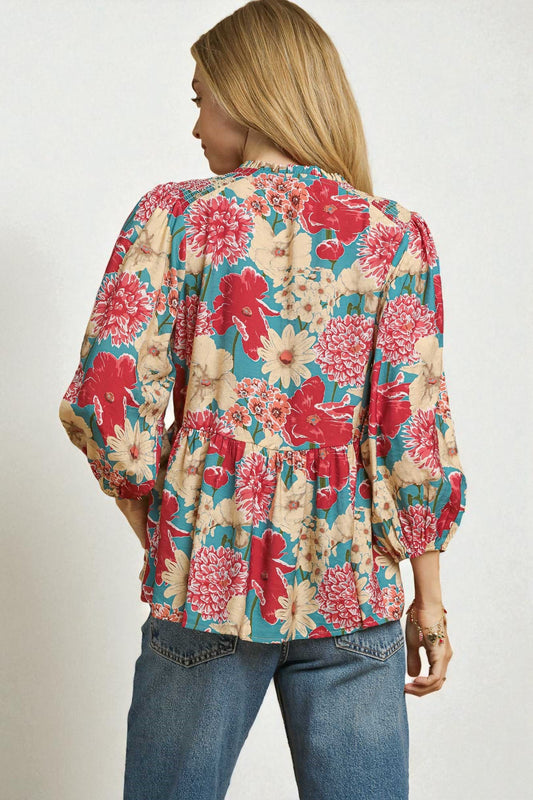 Woman wearing a floral blouse with red and blue flowers on a plain background