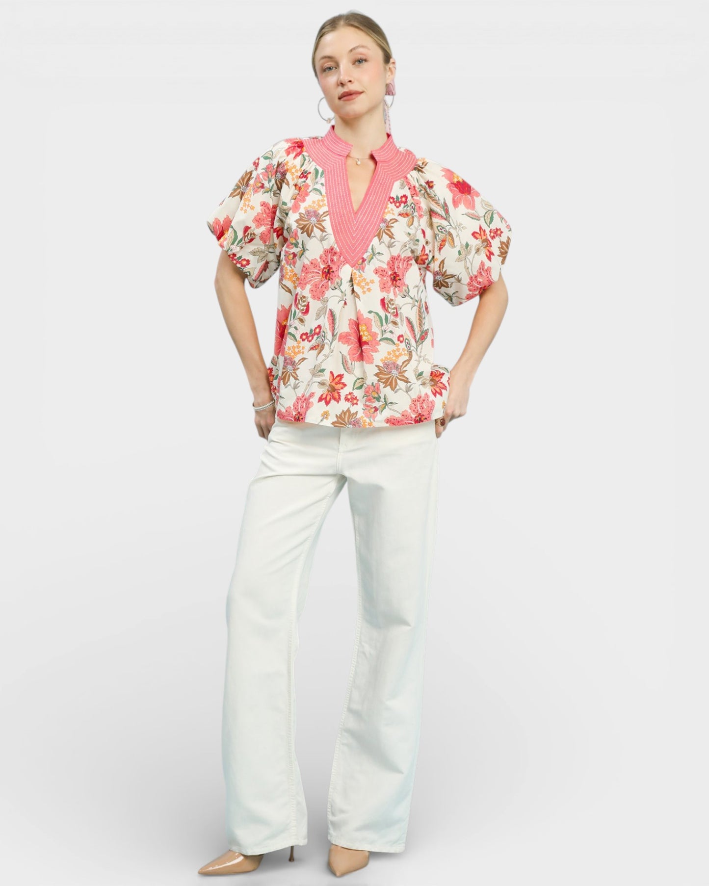 Woman wearing a floral blouse and white pants on a white background