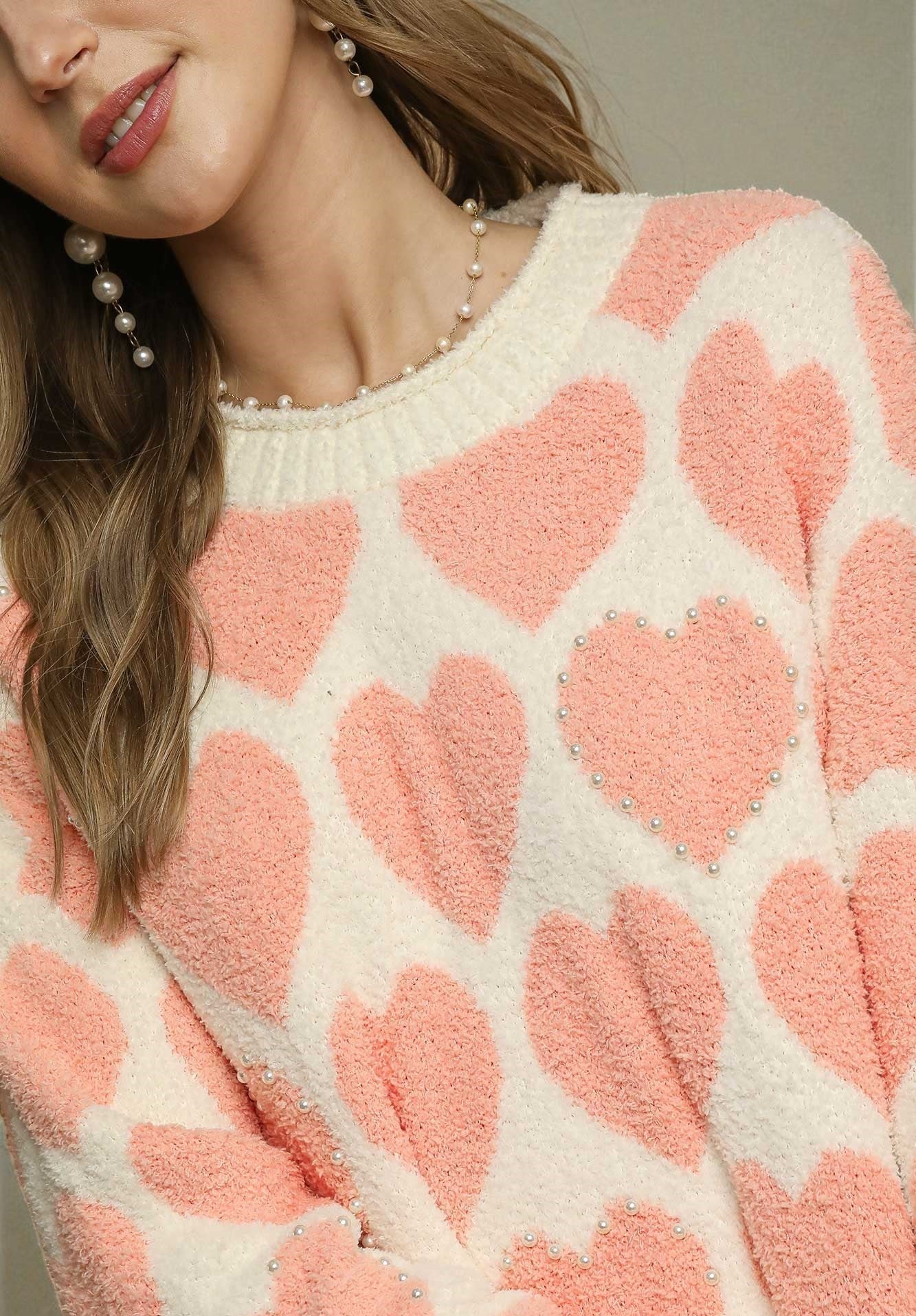 Close-up of a person wearing a cream sweater with pink heart patterns.