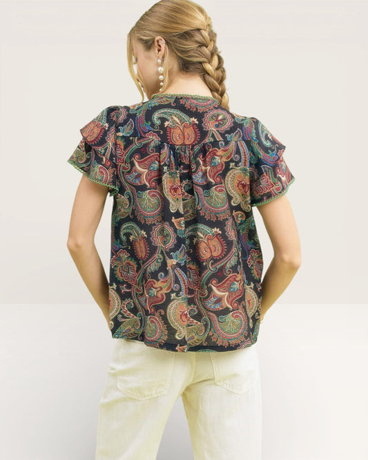 Girl wearing a patterned top and white pants on a plain background