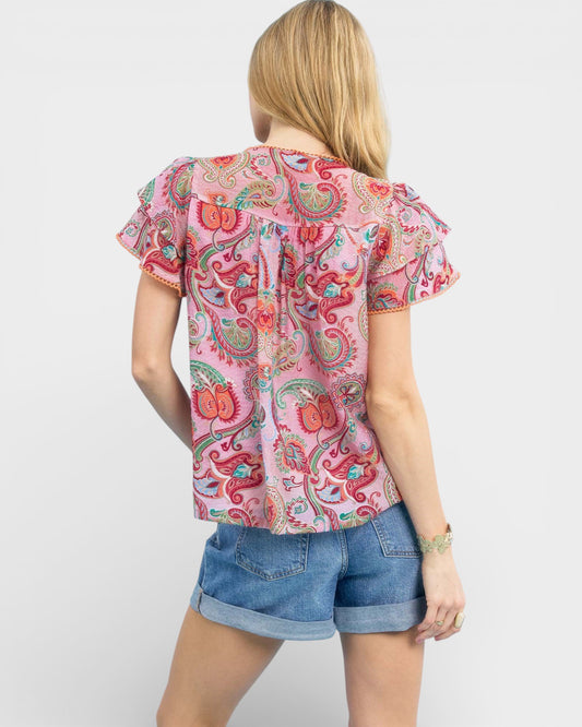 Woman wearing a pink paisley top and denim shorts on a white background