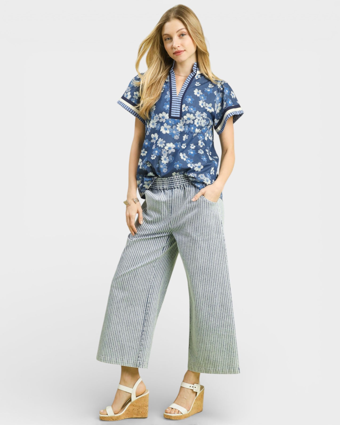 Woman wearing a blue floral blouse and striped pants on a white background