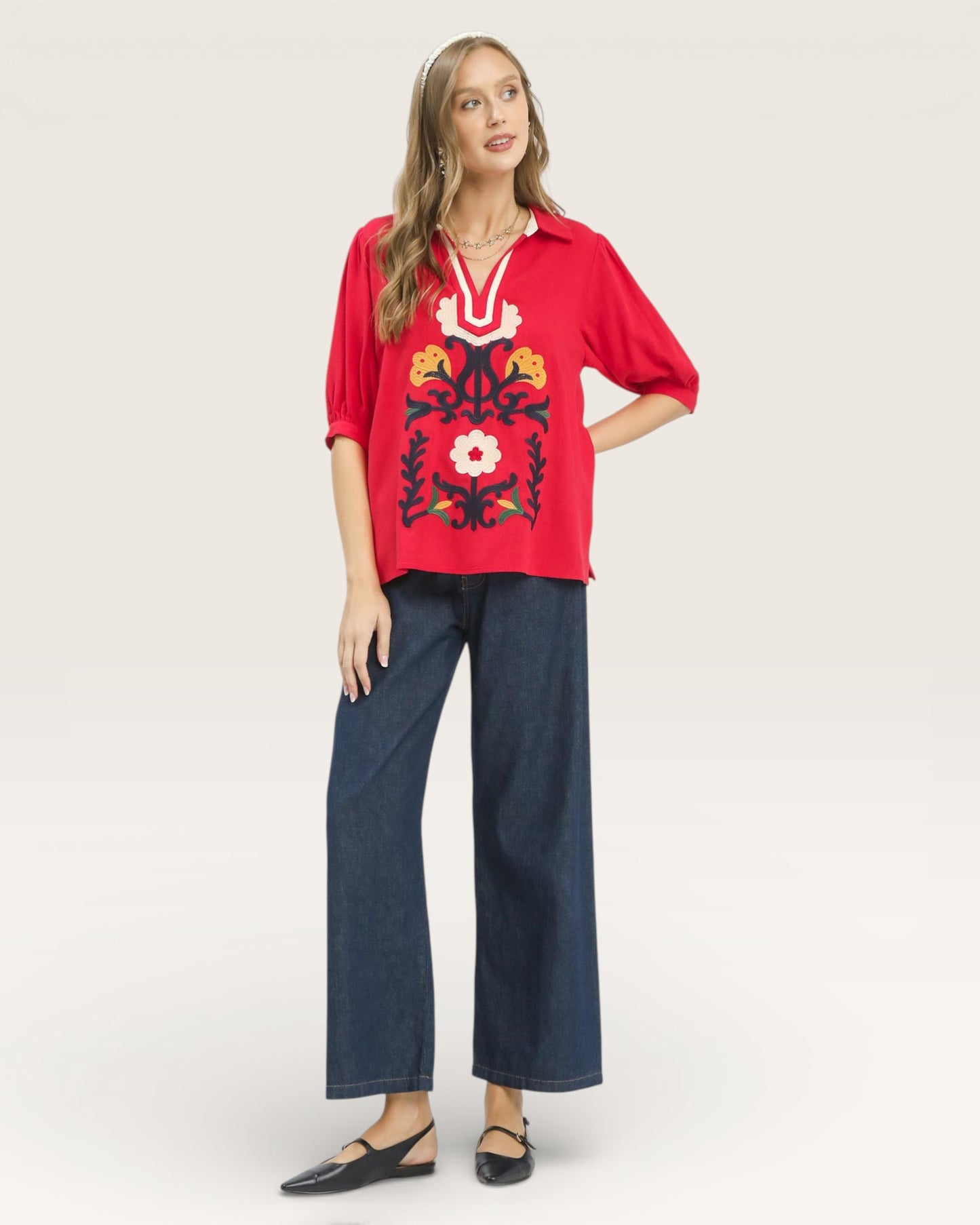 Woman wearing a red embroidered top and blue jeans on a white background