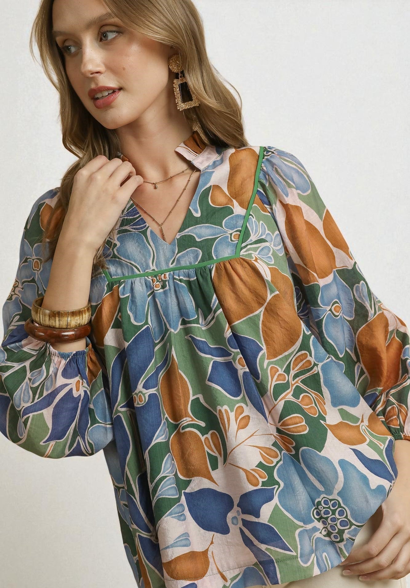 Woman wearing a floral patterned dress with green, blue, and orange colors on a white background.