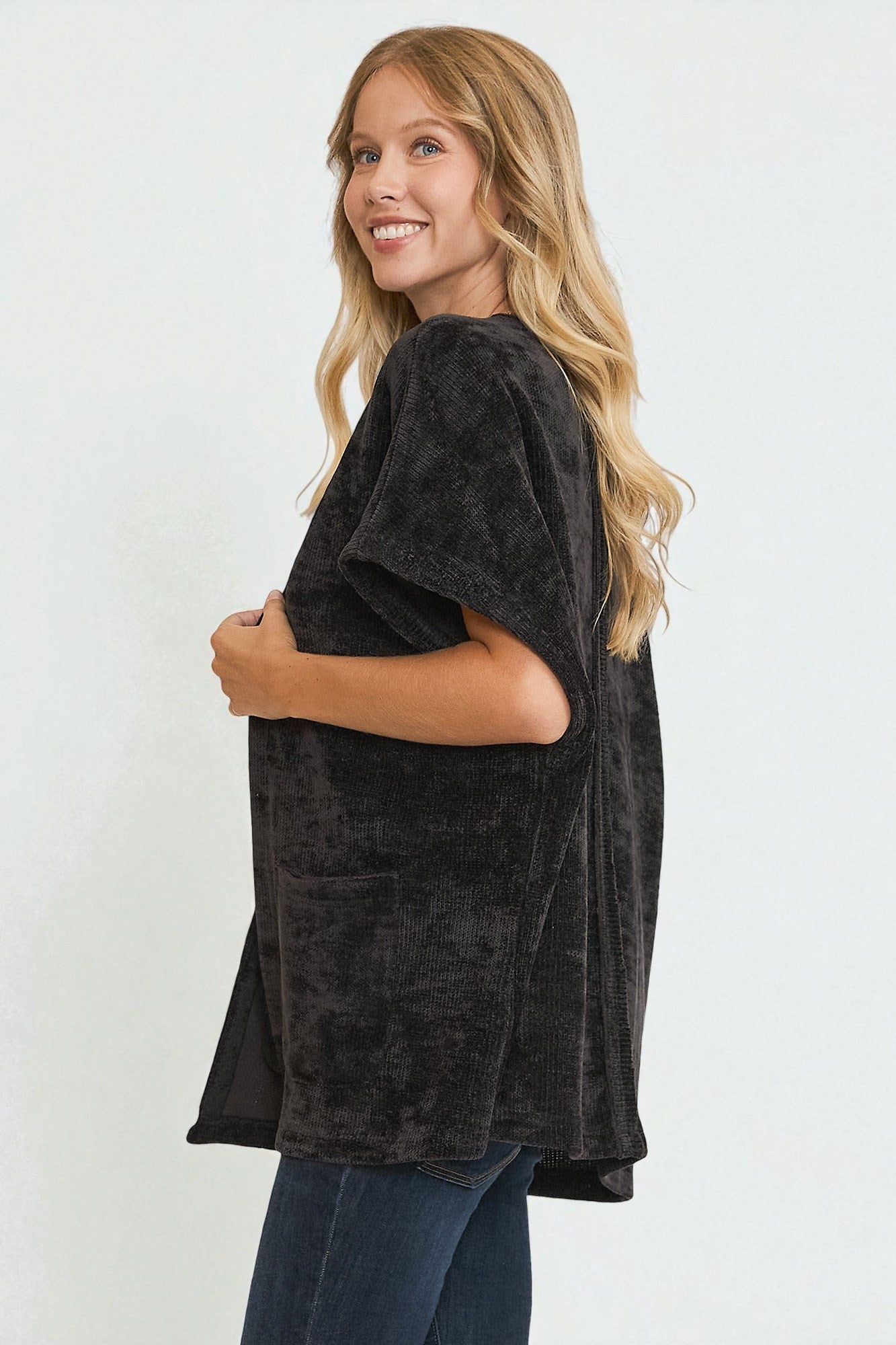 Woman wearing a black tunic over a dark top with blue jeans on a white background