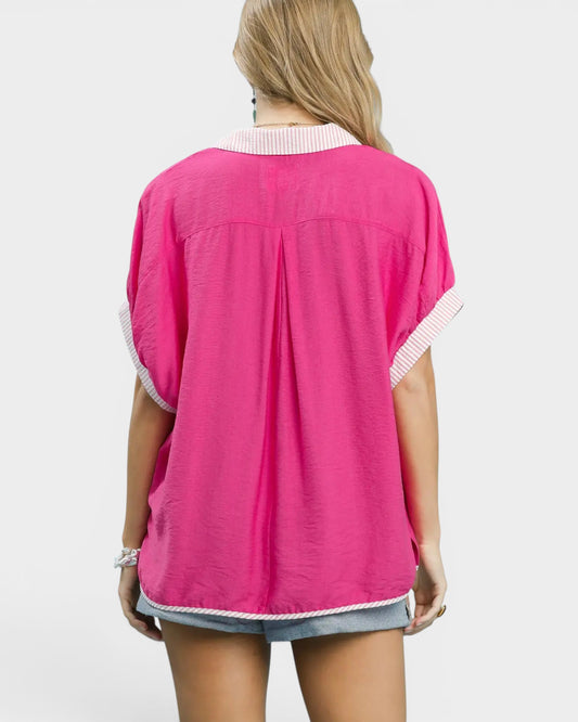 Person wearing a bright pink shirt with white trim on a plain background