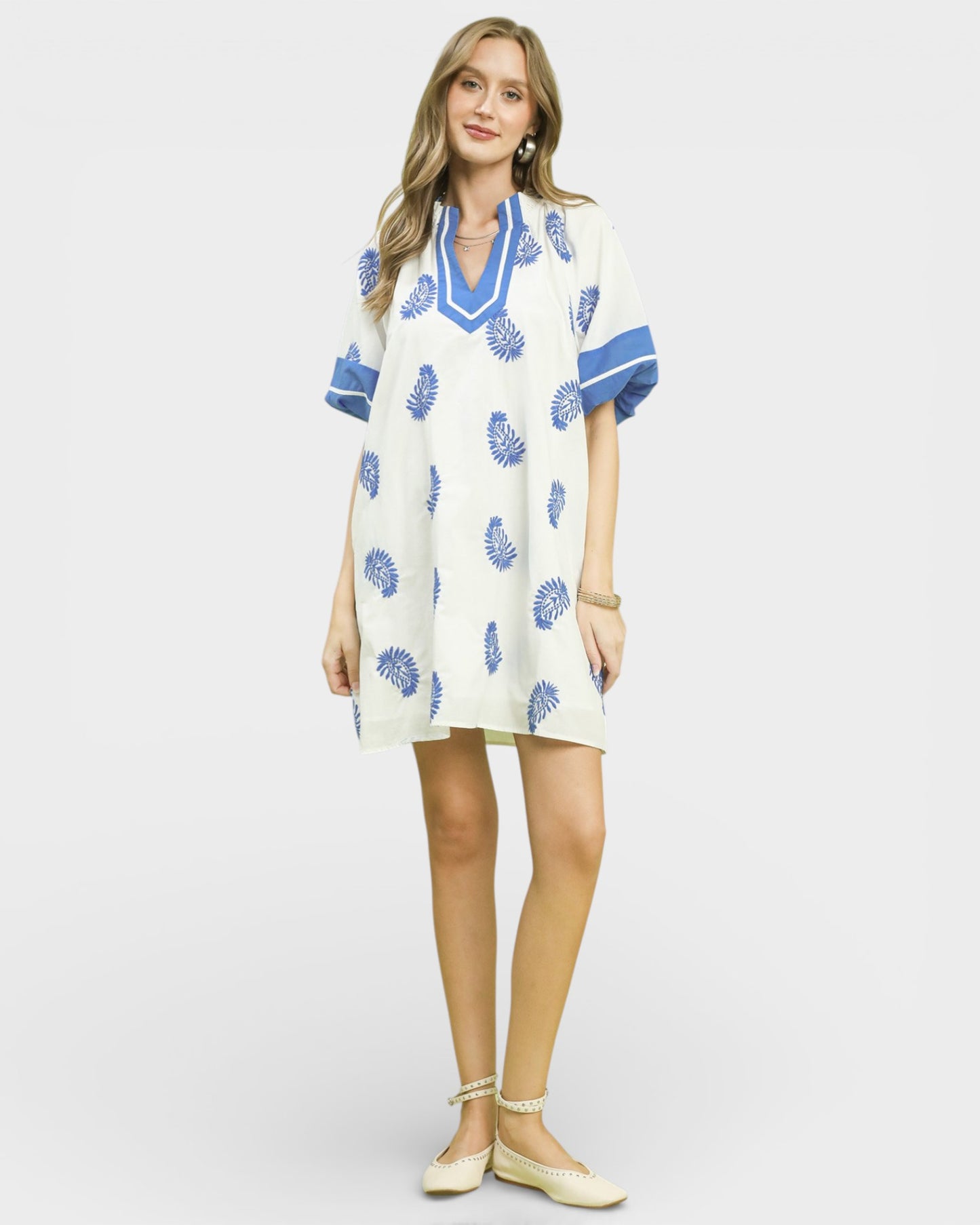 Woman wearing a white dress with blue floral patterns on a plain background