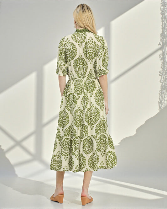 Woman wearing a green and white patterned dress in a bright room with sunlight casting shadows.