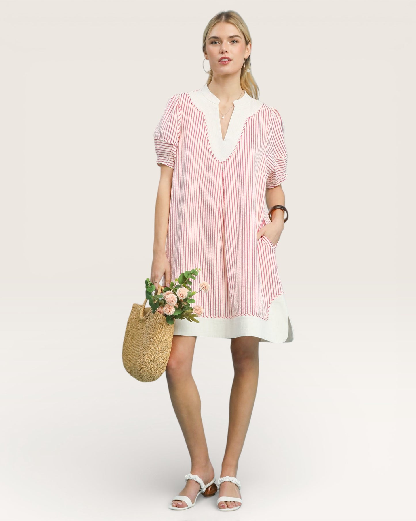 Woman wearing a pink and white striped dress holding flowers against a plain background