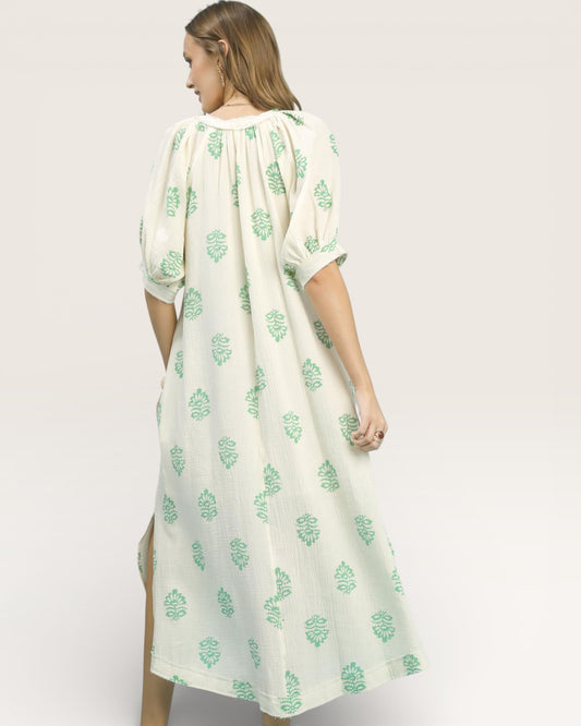 Woman wearing a white dress with green floral patterns on a plain background