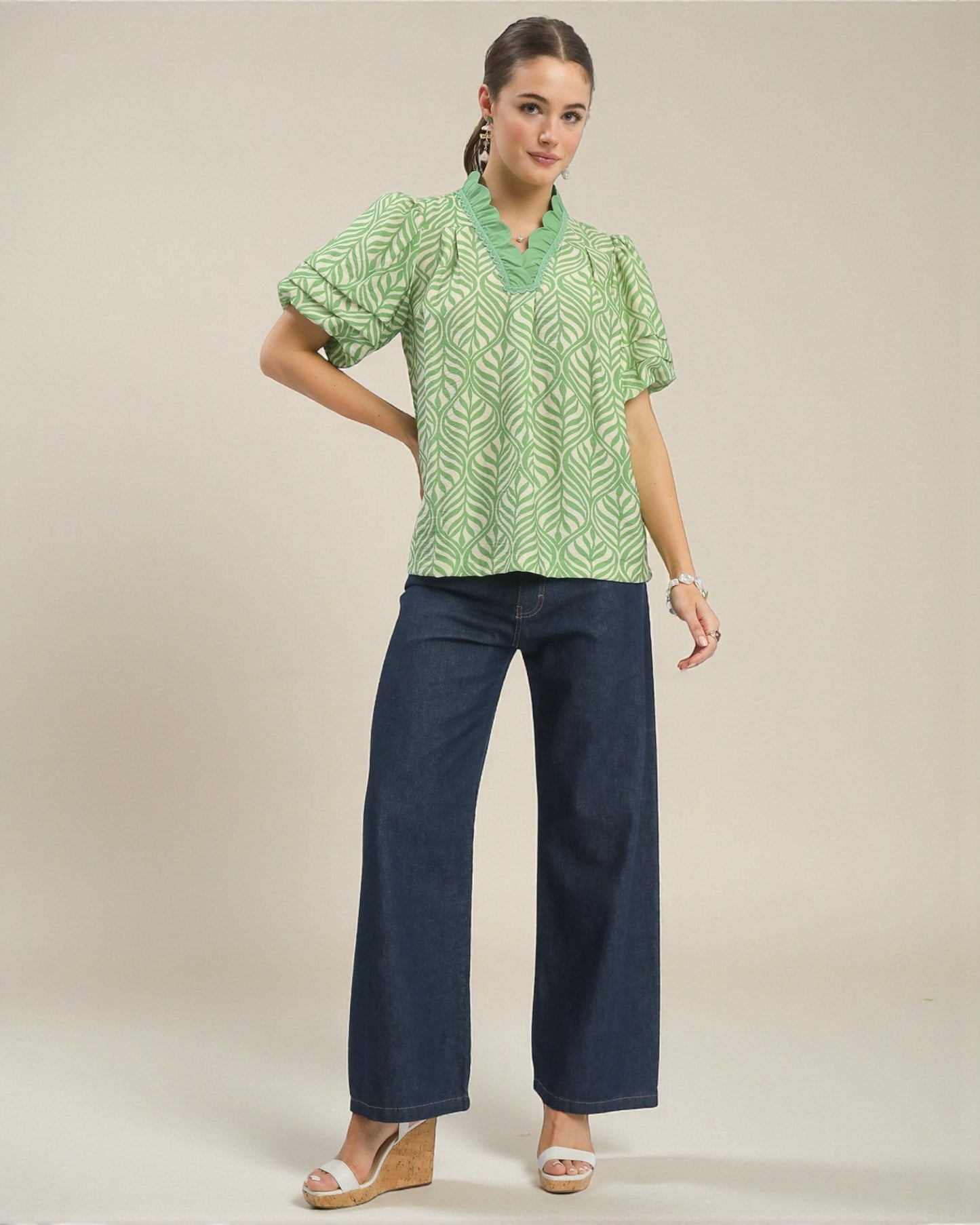 Woman wearing a green patterned blouse and blue pants on a beige background
