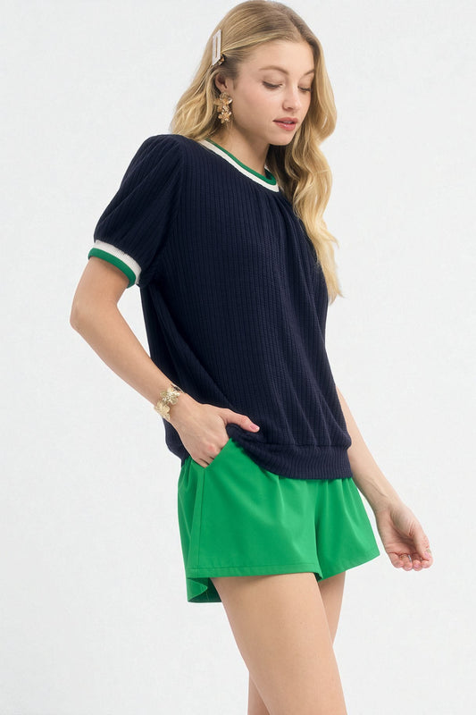 Woman wearing a navy sweater with green trim and a green skirt on a white background