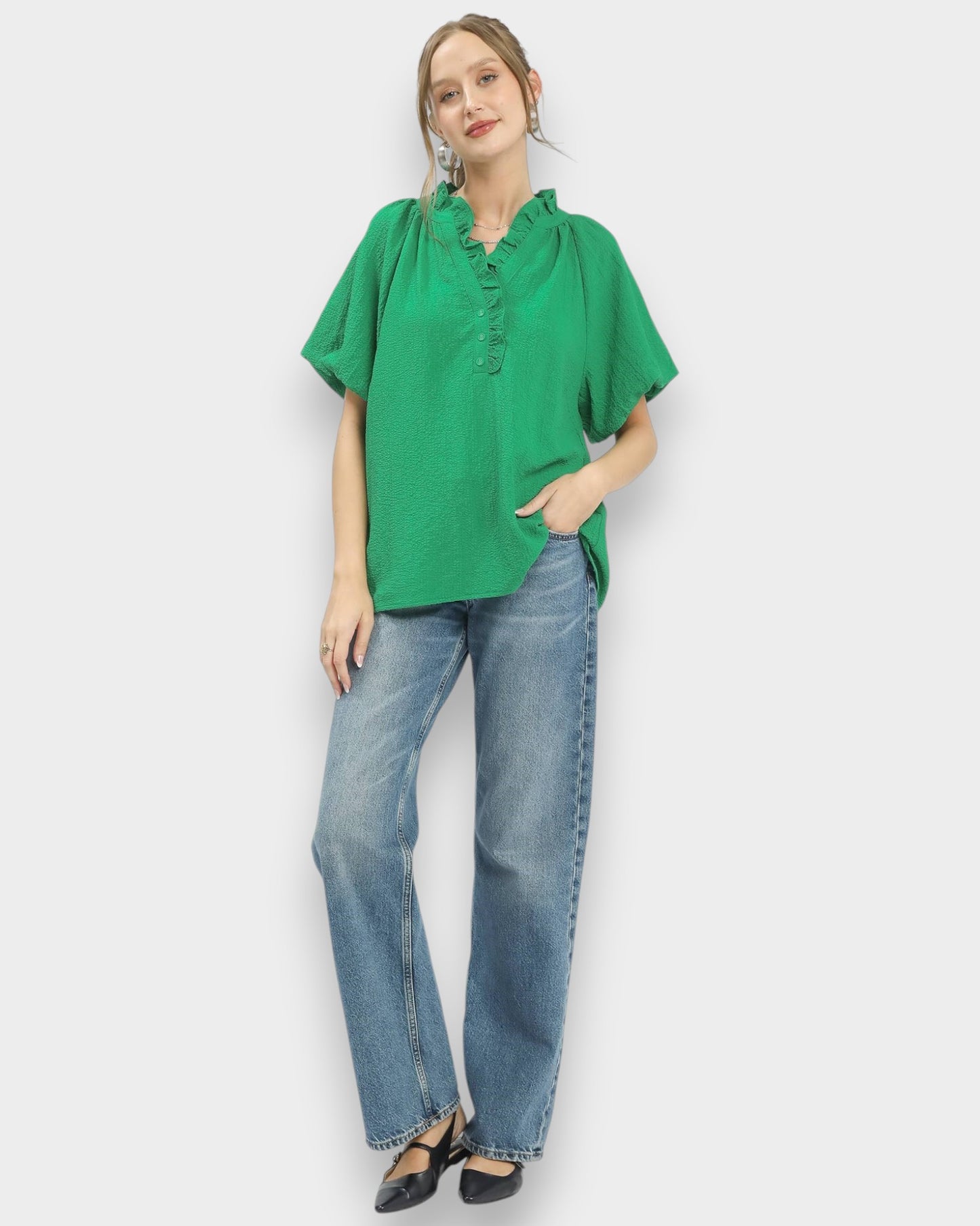 Woman wearing a green top and blue jeans against a white background