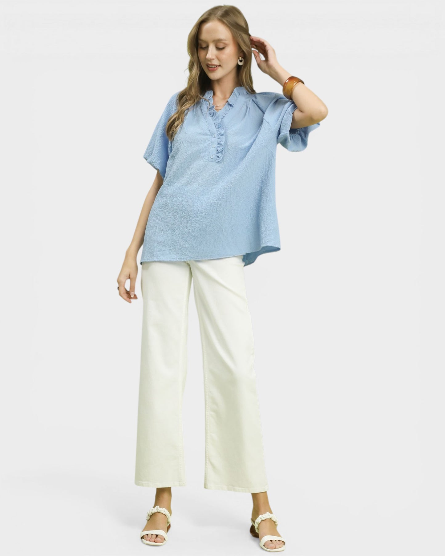 Woman wearing a light blue shirt and white pants on a plain background